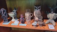 Full shelf view showing all small statues, three owls, glass, and vase in wooden cabinet.