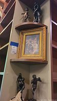 Photo showing one framed artwork and four bronze sculptures arranged on a corner shelf.