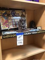 Shelf showing a battery-operated clock with colorful abstract artwork and two boxed board games under it.
