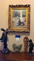 Five-object group shot: two bronze-tone goddess sculptures flanking green planter, carved mask and framed print above