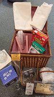 Photo showing contents of wicker basket with incense boxes, cassette tape, candles, glass candle holders, and white cloths