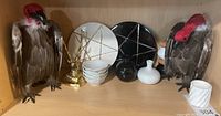 Two decorative vultures, ceramic offering plates with star designs, brass deer figurine, and assorted small ceramic dishes arranged on a wooden shelf.