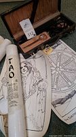 Photo shows the vintage lined case containing the Violetta violet ray wand, power cord, and glass electrode, along with a Tao scroll and a detailed black and white illustration of a woman with tattoos resembling stars and constellations on her arm.