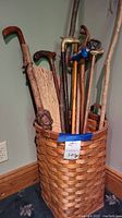 A woven basket filled with various wooden walking canes with different handles and a broom.