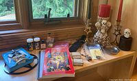 Overview photo showing a variety of ritual items including books, candles, candlesticks, jewelry, statues, and bottles on a wooden surface near window