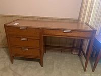 Full front view of the desk showing the four drawers on the left side and the overall wood and laminate construction with metal handles.