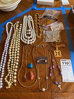 Photo showing all jewelry items on wooden surface including beaded necklaces, gold-tone chain bracelet, pendants, and earrings.