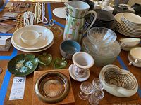 Overview of glassware, ceramic bowls, Andrea by Sadek pitcher, candle holders, plates, and ash trays on wooden table