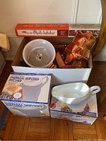 Box of assorted kitchenware items including ceramic bowls, copper pans, and boxes containing thermal serving pitchers.