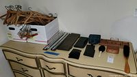 Wide view photo showing wooden hangers, wallets, tie racks, grooming brushes, travel slippers, and a leather tie holder displayed on a dresser top.