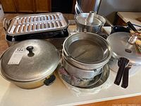 Photo showing multiple aluminum pots with lids and a two-tiered cake pan with central tube placed on kitchen counters.