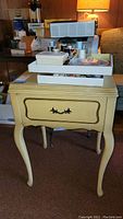 Full view of cream-colored sewing table with white Rotary sewing machine on top, showing legs and drawer.
