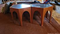 Two hexagonal wooden side tables shown together on a carpet, displaying overall shape and finish.