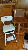 Photo showing wooden swivel bar stool and white metal step ladder chair side by side.