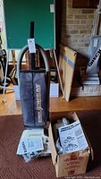 Full view of Eureka Powerline vacuum with instruction manuals and Oreck vacuum with accessories in box.