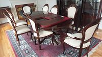 Wide angle image showing all eight wooden dining chairs around a dining table on a patterned rug.