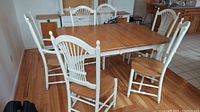 Overall view of the six dining chairs arranged around a matching wooden dining table, showing four standard chairs and two captain's chairs with white painted frames and natural wood seats.