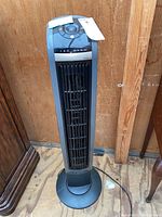 Full view of Lasko black and gray oscillating tower fan standing upright on wooden floor.