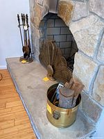 Photo of the brass peacock fireplace screen in the fireplace, brass bucket with firewood and brush, and a partial view of the fireplace tool set on base.