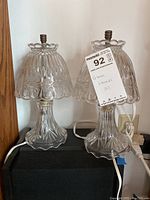 Photo of two matching clear glass lamps with ribbed and scalloped design, metal socket tops, electric cords visible.