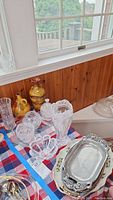 Photo of clear cut glass vases, candy dishes, and ceramic vases on a checkered tablecloth near window