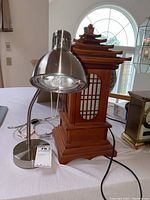 Two lamps on a table: a silver metal desk lamp with flexible neck and a brown Japanese-style wooden lamp with pagoda roof.