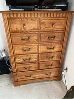 Front view of oak dresser showing six drawers with brass handles and keyhole accents, detailed wood trim on top and scalloped base.
