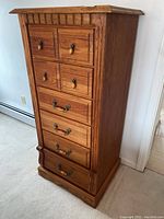 Side perspective of the tall oak lingerie chest showing the decorative top and lower carved base with six drawers.