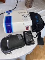 Image showing the Olympus Stylus TG-4 camera original box, battery charger, power adapter, and black soft carrying case.