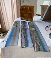 Table display of three elongated paintings and a wooden wall shelf on white cloth