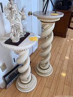 Pair of cream-colored spiral twisted pedestals with gold accents. One pedestal topped with a figurine sculpture.