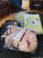 Four quilts in plastic bags shown on floor next to furniture.