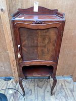 Front view of a tall wooden record cabinet with glass door and decorative details on a wooden floor and panel background.