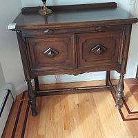 Front view of the wooden sideboard showing two cabinet doors with diamond shaped handles, turned legs, and backsplash on top.