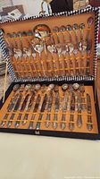 Silverplate flatware set displayed in open storage case with orange interior. Multiple forks, knives, spoons, serving fork and spoons are visible.