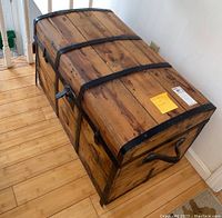 Angled top front side view of the wooden trunk showing metal straps and side handle