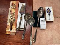 Photo showing two small floral wall art pieces, pie server, two shell-shaped serving spoons, large serving spoon, and boxed blue crystal wine bottle stopper.