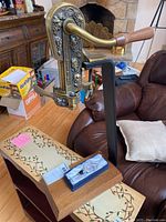 Vintage style wine opener mounted on wooden base with decorative vine pattern and wine bottle stopper in packaging on top of base near leather chair and fireplace.