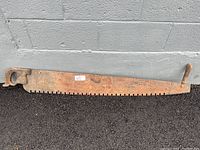 Full view of long rusty two-person tree saw with wooden handles showing blade and teeth condition