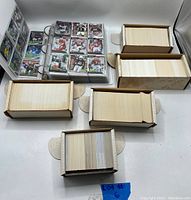 Photo showing an open binder with football cards in plastic sleeves and several open boxes filled with loose cards, mostly football with some baseball cards.