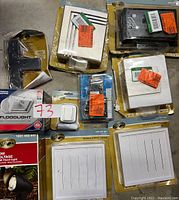 Overview of all items including doorbell units, wall covers in white and black, a Lithonia floodlight and Hampton Bay spotlight in packaging, all untested.