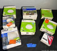 Photo of the lot showing multiple boxed LED lighting products from Halo LED, Commercial Electric, Eaton, and others laid out on a black surface.