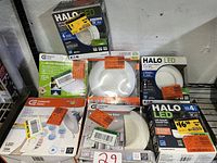 Photo showing multiple boxes of LED down lights and retrofit kits from Halo and Commercial Electric, with visible price tags and labels.