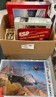 Box containing two Trefl 1000-piece puzzles and two ESP Super Cassette Fun games.