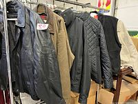 Six men's jackets and vests on hangers, various styles and colors including leather, suede, quilted, fleece.