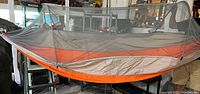 Full side view of orange and beige mesh hammock with mosquito net suspended and supported by poles indoors.