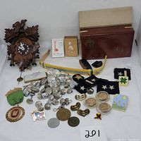 Overall lot photo showing wooden cuckoo clock, military buttons, cloth patches, belt, medallions, pins, a money clip box, and a scout ring