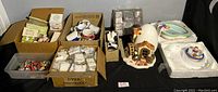 Wide view showing multiple boxes containing keychains, coffee mugs, and several ceramic figurines including a house and pool themed pieces.