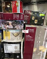 Photo showing multiple boxes of lighting fixtures stacked, including chandelier, string lights, wall sconce, lantern, and pendant light.