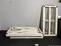 Top view of one shelf panel and several white support poles stacked on a black surface.